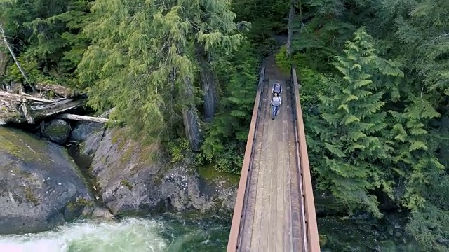 男人和女人夫妇享受户外自然徒步通过森林和横跨桥梁覆盖河流。空中高角度视图视频素材