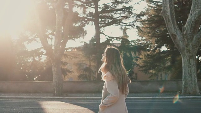 迷人的年轻女子走在公园附近的路在日落。女性享受着明媚的春日，探索着城市视频下载