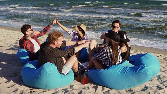 一群年轻的朋友坐在海滩上，玩得很开心，互相击掌在一个夏天的晚上在慢镜头视频下载
