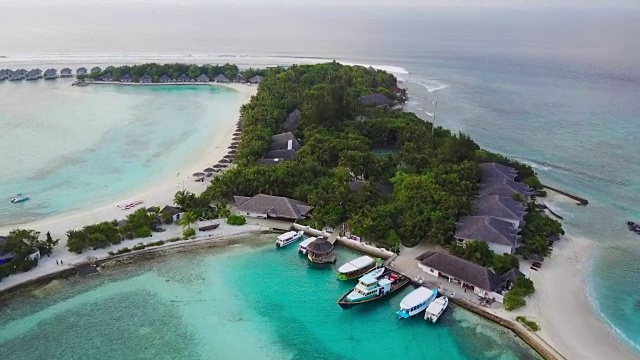 马尔代夫热带岛屿度假酒店的鸟瞰图，白色的沙棕榈树和绿松石般的印度洋，码头，船只和渡轮的无人机镜头，4k视频下载