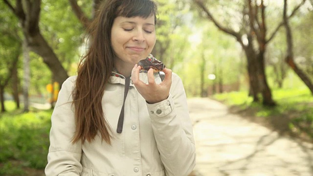 年轻女子在街上吃巧克力甜甜圈。视频素材