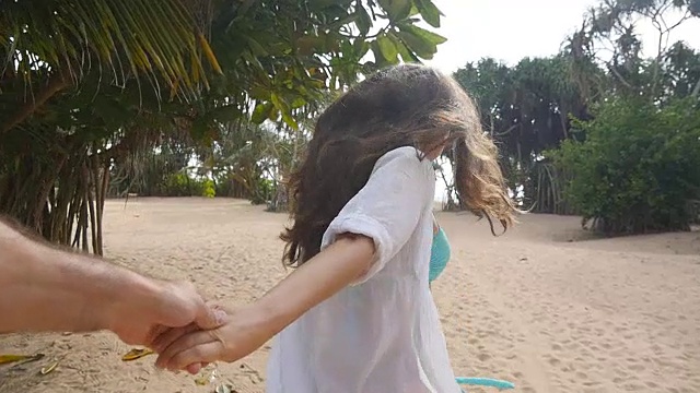女孩牵着男人的手，在热带异国的海滩上奔向大海。跟着我拍的一个年轻女人拉着她的男朋友在海边。暑假或假期。的观点。观点慢动作视频素材