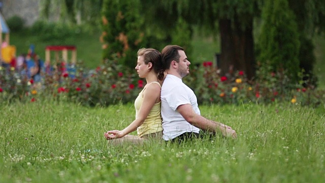 人们在做运动前做伸展运动。年轻的瑜伽教练在城市公园的草地上练习。成功的白人男女正在休息。视频下载