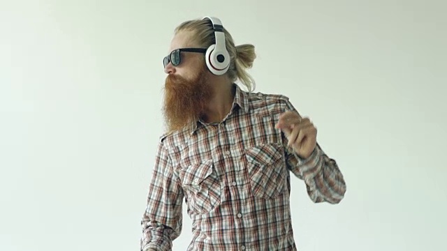 慢动作的快乐的年轻胡子男子戴着太阳镜和耳机跳舞和听音乐的白色背景视频素材