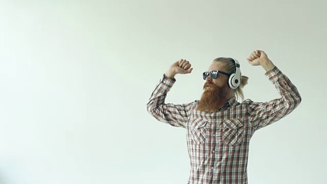 慢动作的快乐的年轻胡子男子戴着太阳镜和耳机跳舞和听音乐的白色背景视频素材