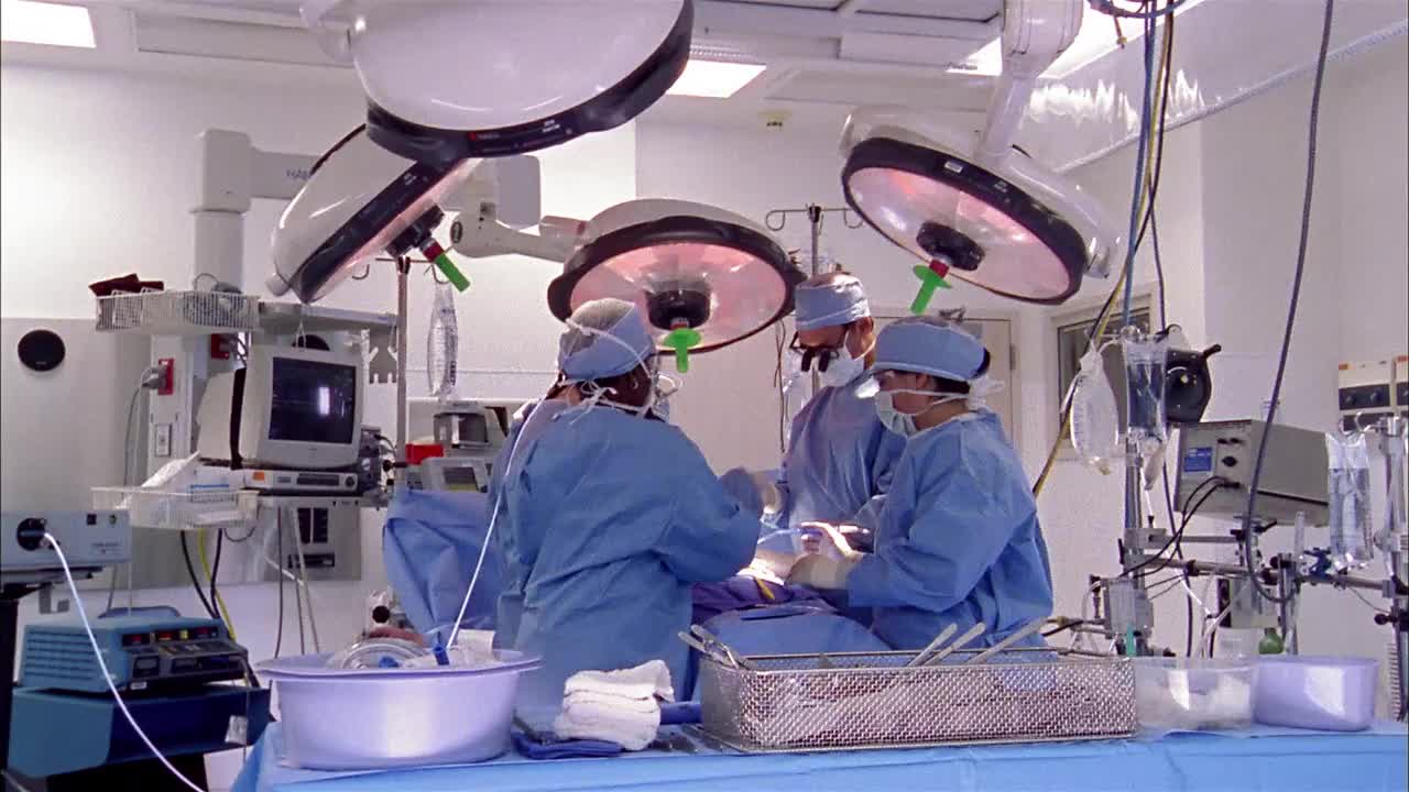 宽镜头摄影车拍摄了在手术台上为病人工作的男性和女性周围的医疗设备视频素材