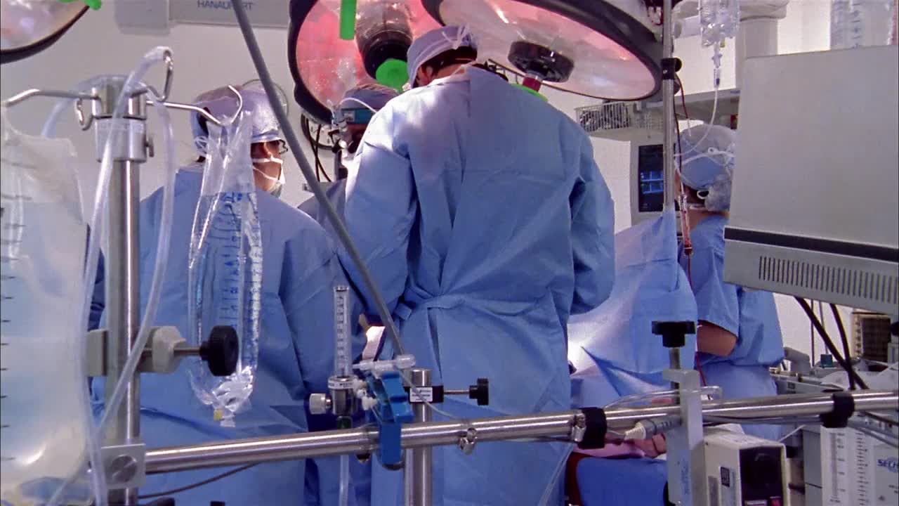 中型摄影车拍摄了经过医疗设备和周围的男性+女性工作在病人/宽镜头手术室视频素材