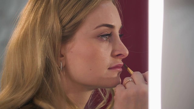 漂亮的金发女人在她的嘴唇上化妆的特写肖像。视频素材