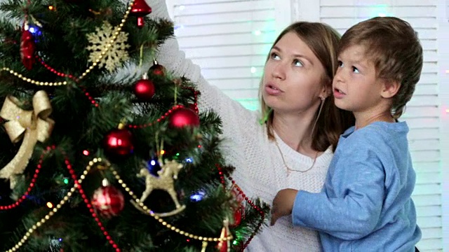 妈妈和儿子在家里装饰圣诞树。视频素材