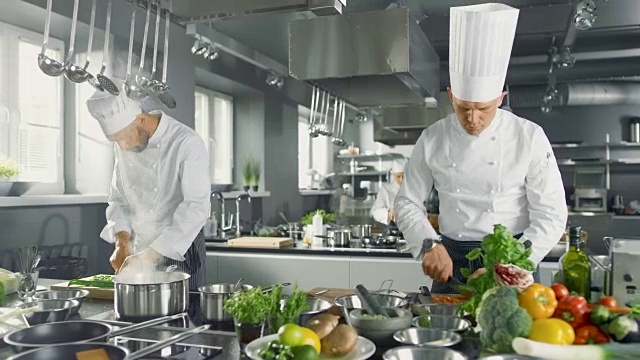 两个著名的厨师在一个大餐厅的厨房团队工作。蔬菜和配料无处不在，厨房看起来很现代，有很多不锈钢。视频素材