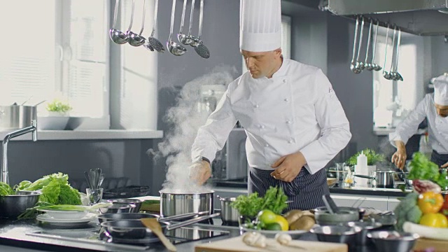 一家大餐厅的著名厨师在厨师的帮助下准备菜肴。现代厨房采用不锈钢材质，配料丰富。视频素材