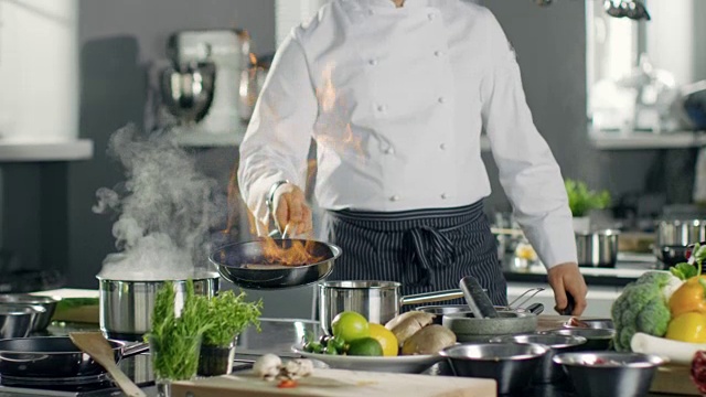 专业厨师在平底锅上烧油。烧过的烹饪风格。他在一个现代厨房工作，里面有很多食材。视频素材