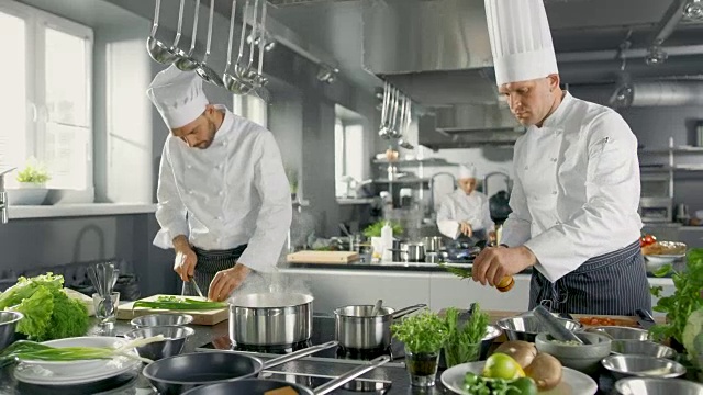 两个著名的厨师在一个大餐厅的厨房团队工作。蔬菜和配料到处都是，厨房看起来现代与大量的不锈钢。视频素材