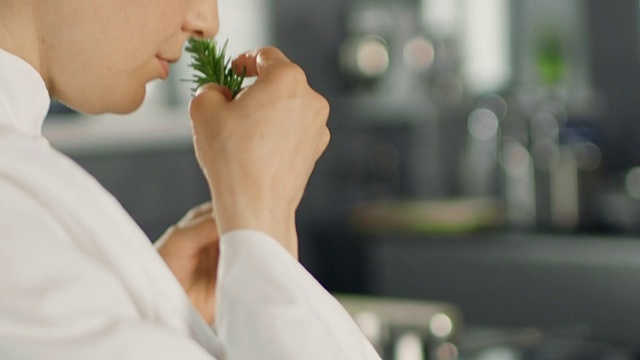 美丽年轻的女厨师闻到装饰香料植物。视频素材