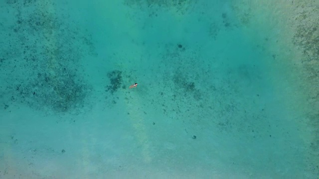 在热带岛屿度假胜地的环礁上，航拍镜头正越过一个穿着比基尼的迷人女子，她漂浮在清澈的海水中。漂亮性感的女孩在印度洋游泳视频下载