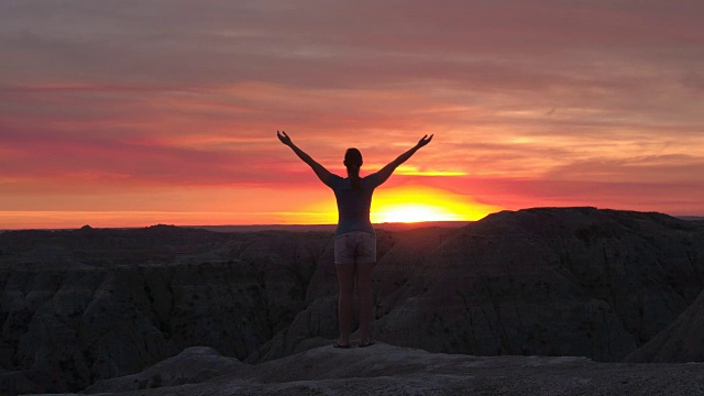慢镜头:日落时分，放松的女子向粉红色的天空举起双臂视频素材