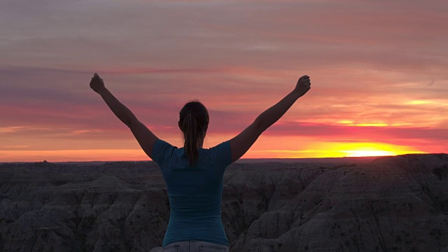 特写:在山顶上，一个快乐的年轻女子在庆祝粉红色的日落视频素材