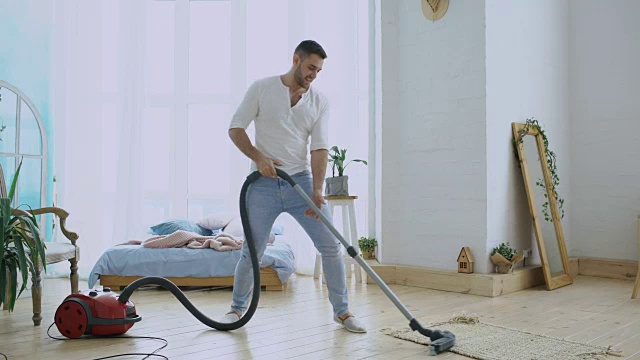 一个年轻人和吸尘器一起打扫屋子，跳舞的样子像个吉他手视频素材
