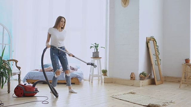 年轻女子有乐趣打扫房子与吸尘器跳舞和唱歌在家里视频素材