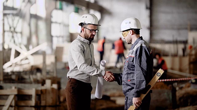 两名男子在现场讨论项目计划。带安全帽的工人在工地背景上共同施工的侧面图视频素材