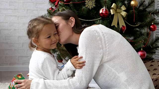 年轻漂亮的母亲手拿礼盒，拥抱并亲吻她的小女儿视频素材