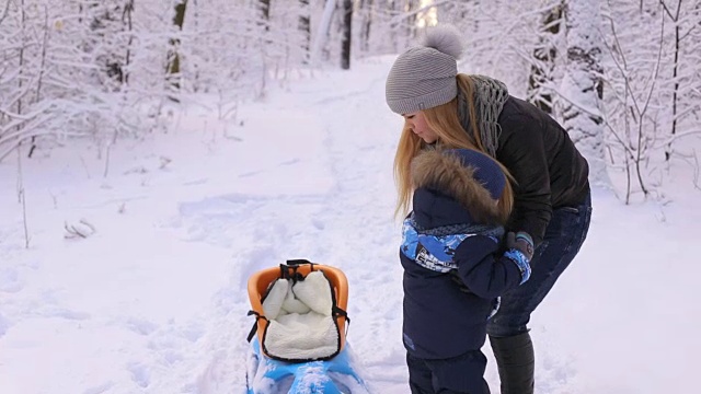 妈妈和儿子带着雪橇在冬季公园散步。视频素材