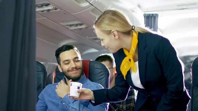 空姐给西班牙帅哥端咖啡。他们在机上。商务舱的一个商业航空内部可见。视频素材