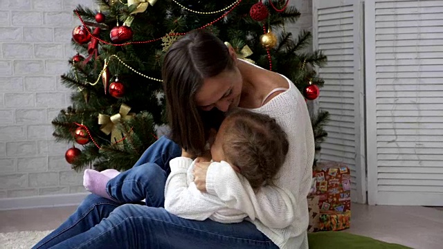 快乐的母亲与她的孩子女儿旁边的圣诞树玩得开心视频素材