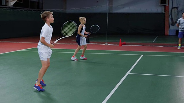 一队男孩和女孩在室内球场打网球。年轻球员练习视频下载