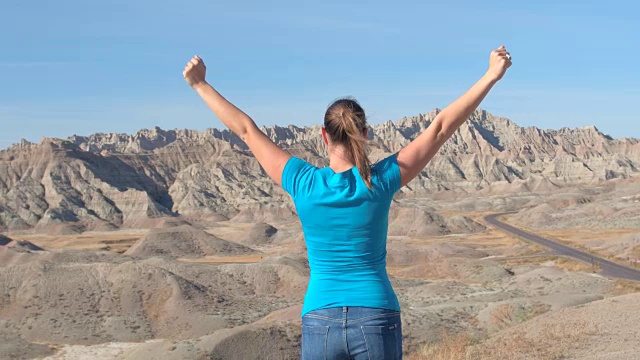特写:在Badlands山顶，快乐的女旅行者向天空举起手臂视频素材