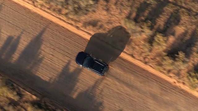 空中特写:飞过黑色越野车行驶在尘土飞扬的沙漠道路上视频素材