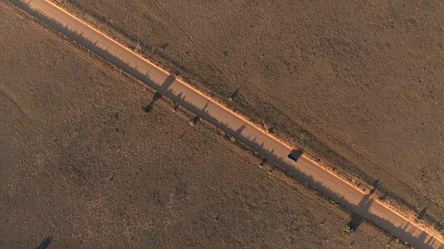 空中镜头:一辆黑色SUV正行驶在阳光明媚的沙漠里的土路上视频素材