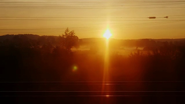 黎明从一列行驶的火车上看到的景象。树木和建筑物的剪影在初升的太阳的背景下迅速闪动视频素材