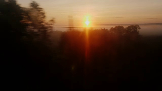 清晨的路上。从火车窗口望出去的景色——冉冉升起的太阳，山谷里的树木和雾气视频素材