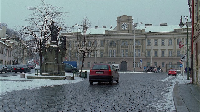 在冬天的苏黎世，红色Mini Cooper行驶在砖车道上，朝着有时钟的建筑驶去视频下载