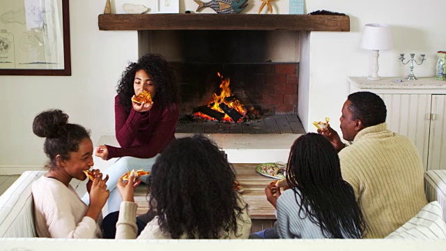 一家人坐在休息室的沙发上，旁边是篝火，吃着披萨视频素材