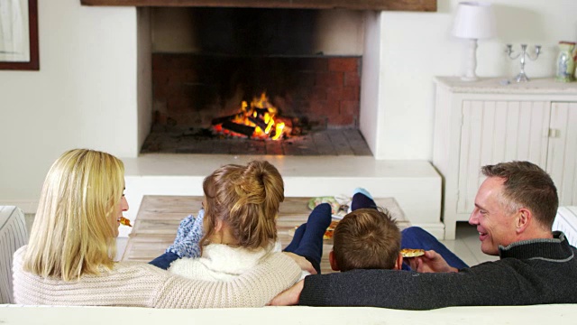 一家人坐在休息室的沙发上，旁边是篝火，吃着披萨视频素材