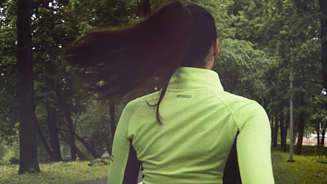 年轻的跑步者深色头发的女人穿着绿色的衬衫在公园跑步视频素材