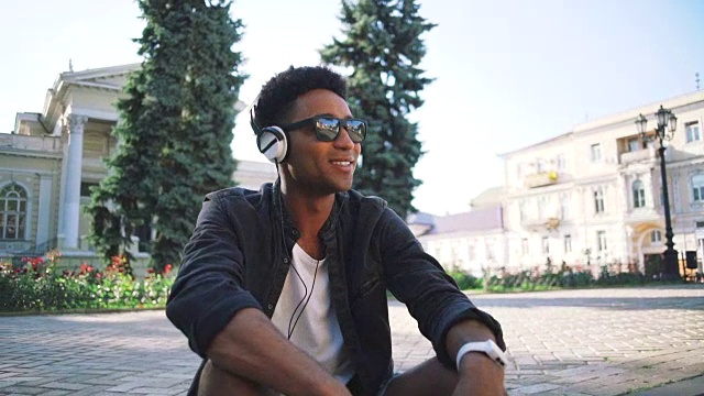 这是一幅年轻时髦的黑人男子的肖像，他戴着白色耳机和太阳眼镜在市中心的户外跳舞，尽情玩乐视频素材