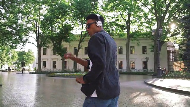 年轻时髦的黑人男子戴着白色耳机和太阳眼镜在市中心的户外跳舞，玩得很开心视频素材
