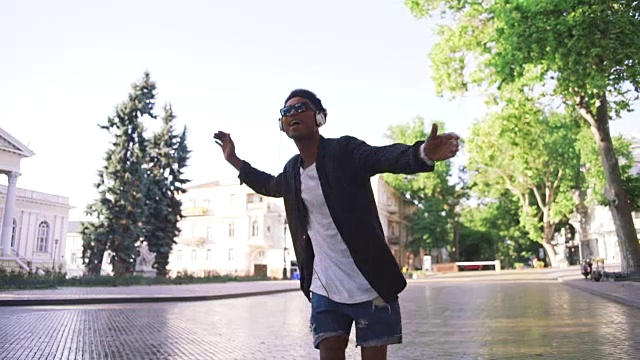 年轻时髦的黑人男子戴着白色耳机和太阳眼镜在市中心的户外跳舞，玩得很开心视频素材