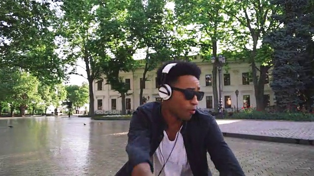 年轻时髦的黑人男子戴着白色耳机和太阳眼镜在市中心的户外跳舞，玩得很开心视频下载