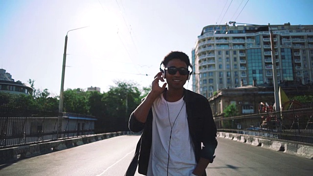 年轻时髦的黑人戴着白色耳机和太阳眼镜，在城市的户外散步和跳舞，玩一些有趣的慢动作视频素材