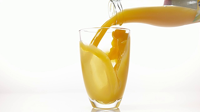在白色背景下，将橙汁倒入玻璃中，慢动作4K视频素材