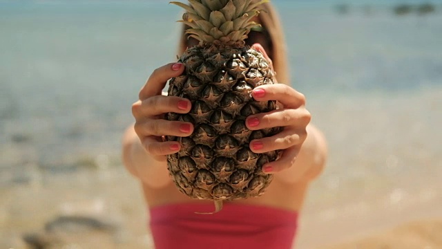 夏天，年轻女子捧着菠萝站在沙滩上视频素材