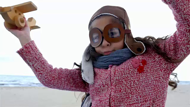 戴着飞行员帽的小女孩在蓝天下玩木制飞机视频素材