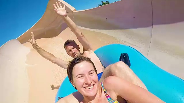 在阳光明媚的日子里，一名男子和一名年轻女子在水上乐园玩水上滑梯视频下载