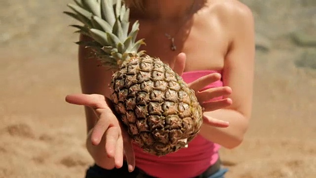 一名身穿粉色t恤的女子在沙滩上卷菠萝水果视频素材