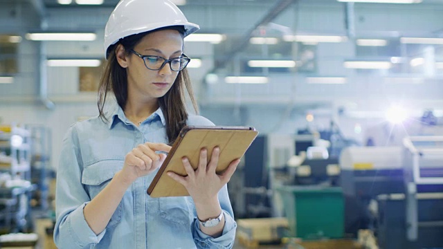 戴安全帽的女工业工程师在大工厂里使用平板电脑。视频素材