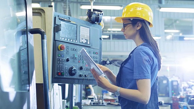 在大型工业工厂中，从事带控制面板的数控机床安装/编程的专业女操作员。视频素材